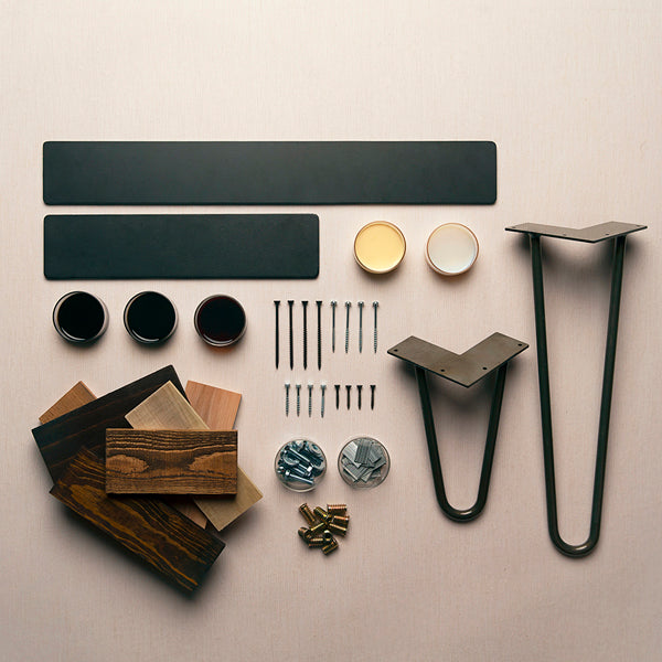 Flat lay of DIY furniture hardware featuring two black metal legs, screws, bolts, three wood stains, two small paint cans, and assorted reclaimed wood samples on a light surface for bar-height dining table assembly.