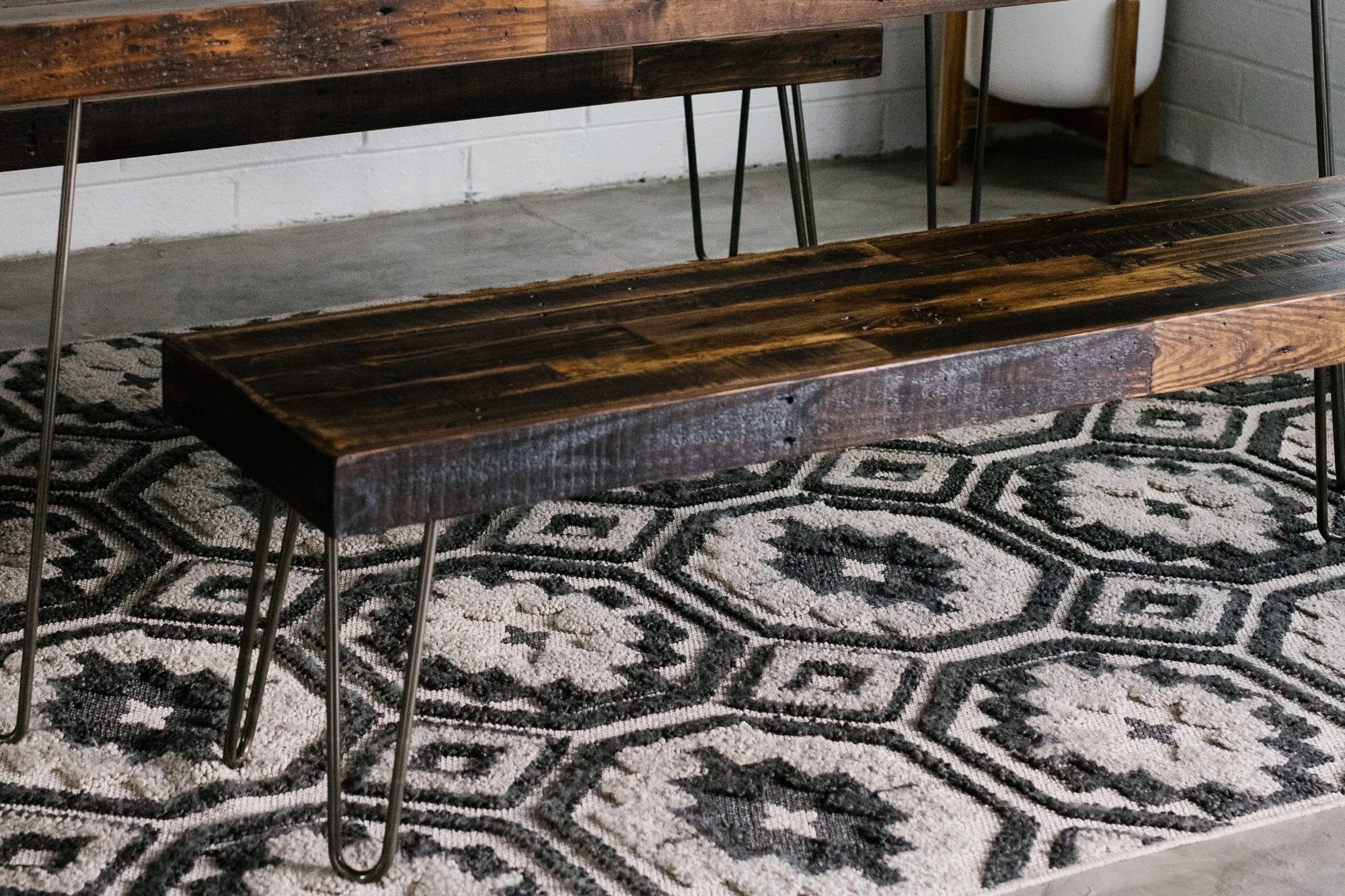 Handcrafted in Arizona, this reclaimed wood narrow bench features sleek steel hairpin legs and rests on a geometric black-and-white rug. Ideal as a kitchen island seat or restaurant table accent, it fuses sustainability with lasting quality.