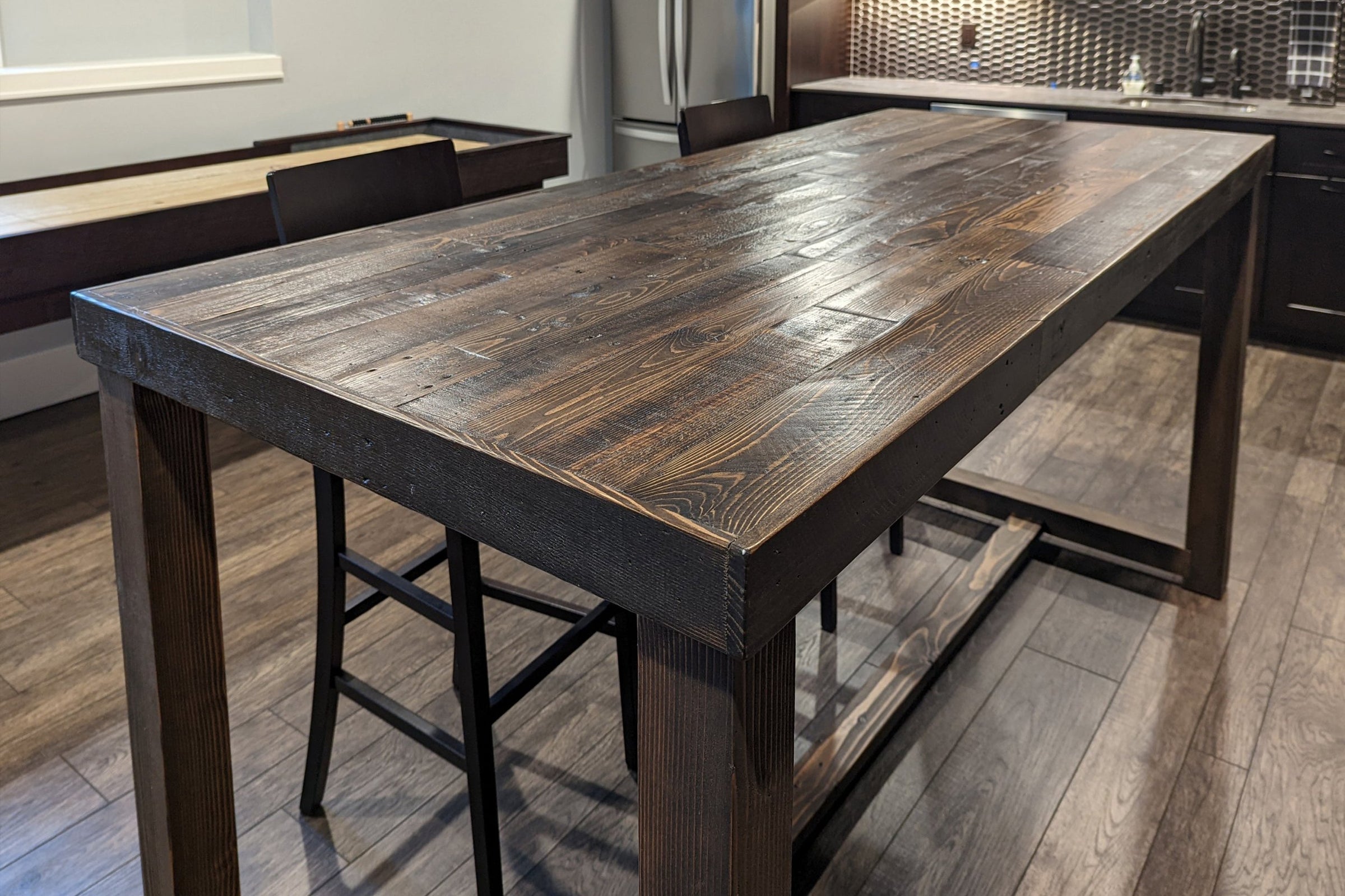 This handcrafted Sequoia bar-height table, made from sustainably sourced reclaimed wood with a rich dark finish, anchors a modern kitchen. Surrounded by high chairs, this durable reclaimed wood furniture exudes enduring quality.