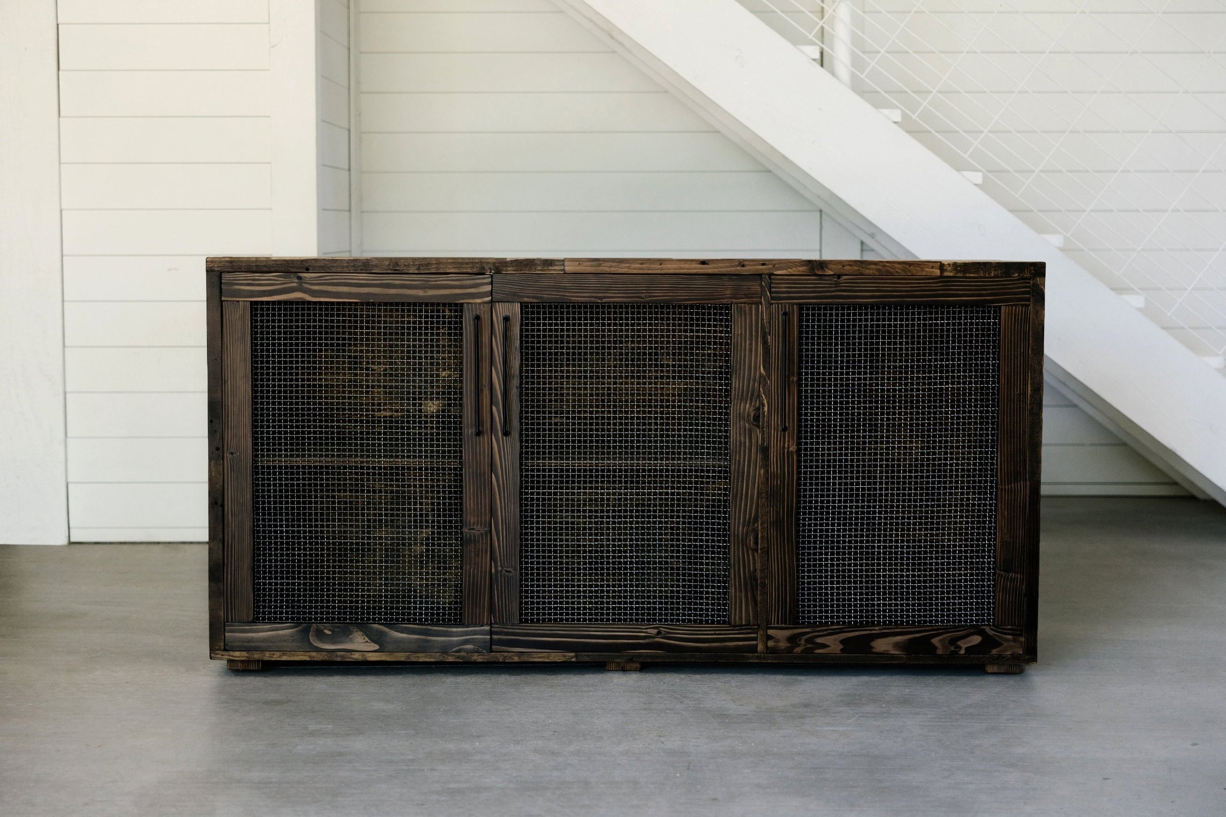 This reclaimed wood sideboard, handcrafted in Arizona, features three mesh-front doors and stands elegantly beside a staircase. Ideal as a narrow table or for reclaimed wood furniture enthusiasts seeking lasting quality.