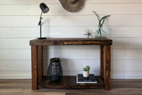 Showcasing timeless craftsmanship, this handcrafted Arizona reclaimed wood narrow console table stands against a white shiplap wall, topped with curated décor. The sturdy shelf below features books, a cactus, and a woven storage basket.