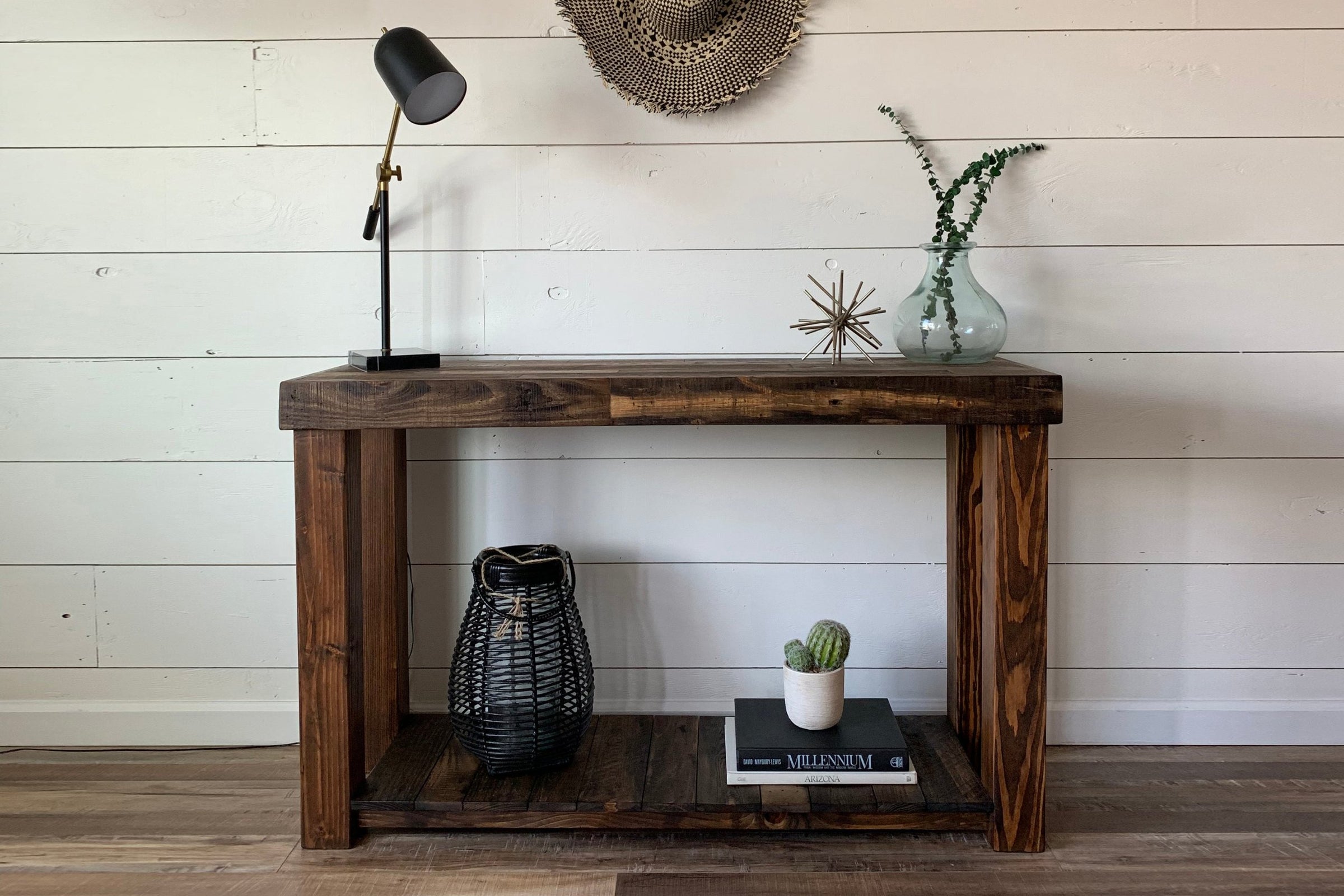 Showcasing timeless craftsmanship, this handcrafted Arizona reclaimed wood narrow console table stands against a white shiplap wall, topped with curated décor. The sturdy shelf below features books, a cactus, and a woven storage basket.