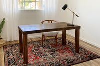 Experience a warm, inviting workspace featuring a handcrafted, reclaimed wood desk—expertly made in Arizona. Paired with a cushioned wooden chair and sleek black lamp, this office showcases enduring quality and sustainable materials.