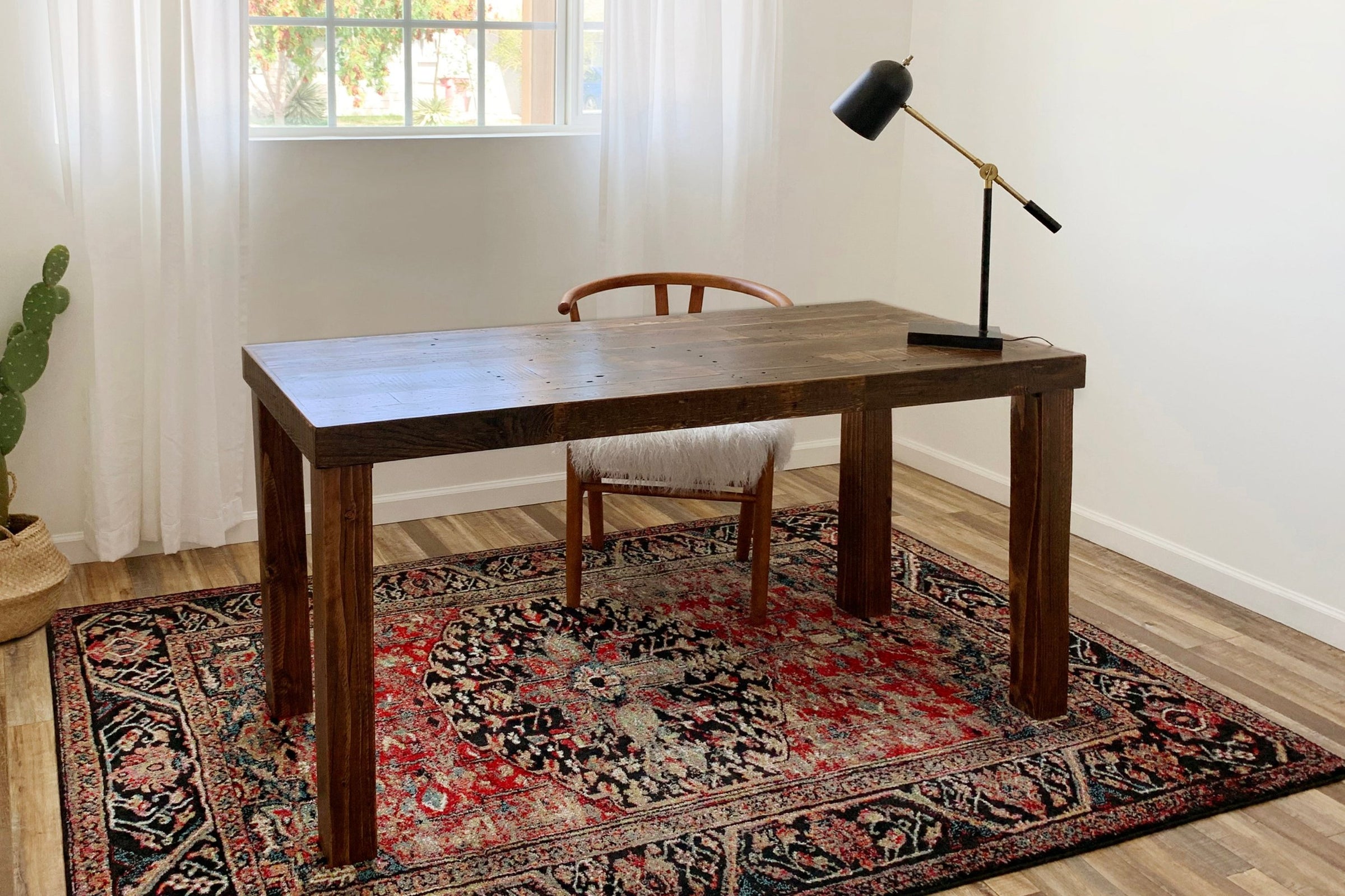 Experience a warm, inviting workspace featuring a handcrafted, reclaimed wood desk—expertly made in Arizona. Paired with a cushioned wooden chair and sleek black lamp, this office showcases enduring quality and sustainable materials.