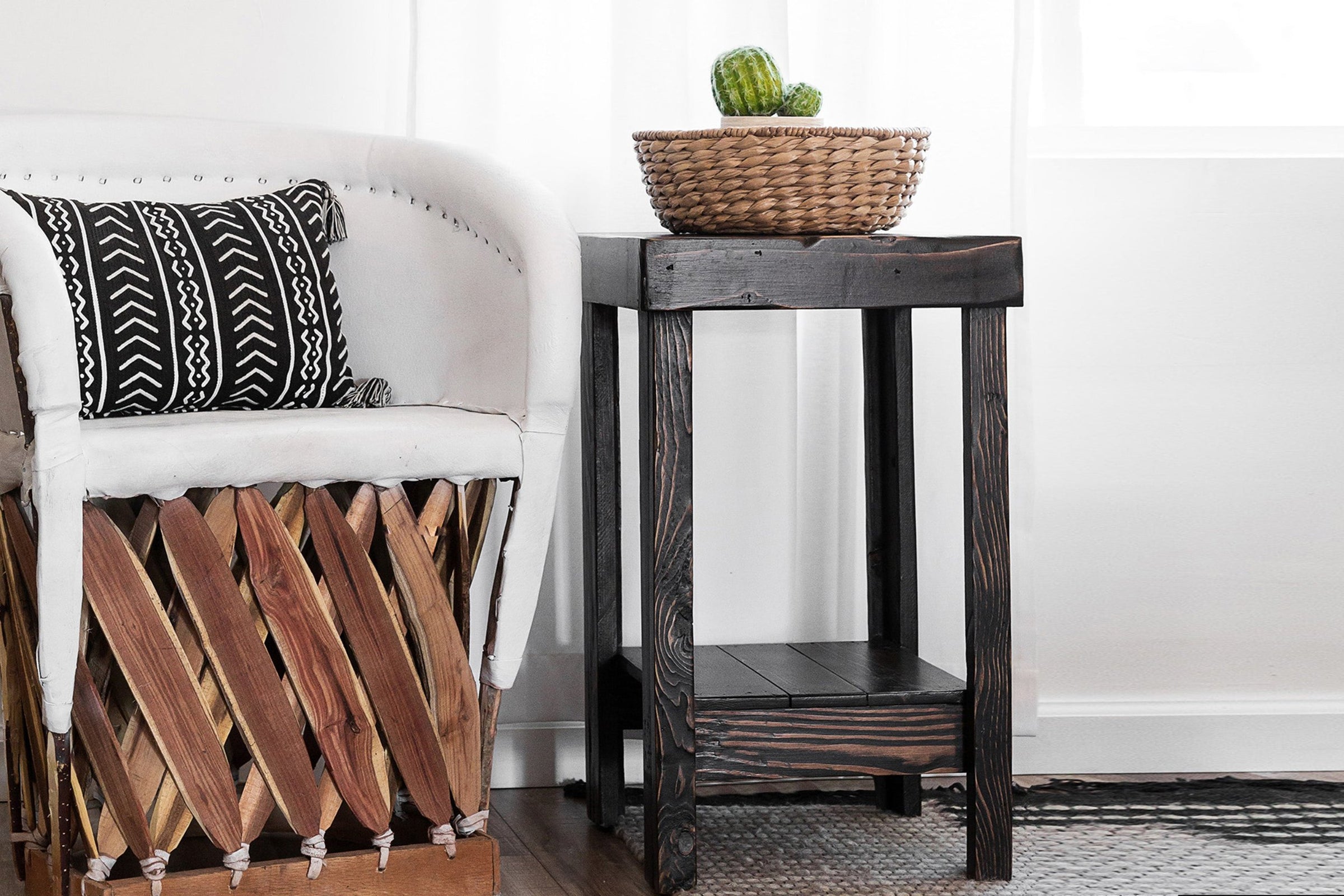 A white armchair with black and white cushions pairs beautifully with a handcrafted solid reclaimed wood side table, perfect as a narrow bar table or accent piece. A woven basket with green gourds adds artisanal charm.