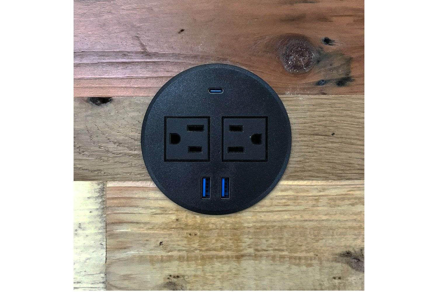 A round black power outlet with two standard sockets, two USB ports, and a USB-C port is seamlessly integrated into a handcrafted reclaimed wood Sequoia bar-height table—an enduring piece of sustainable furniture from Arizona.