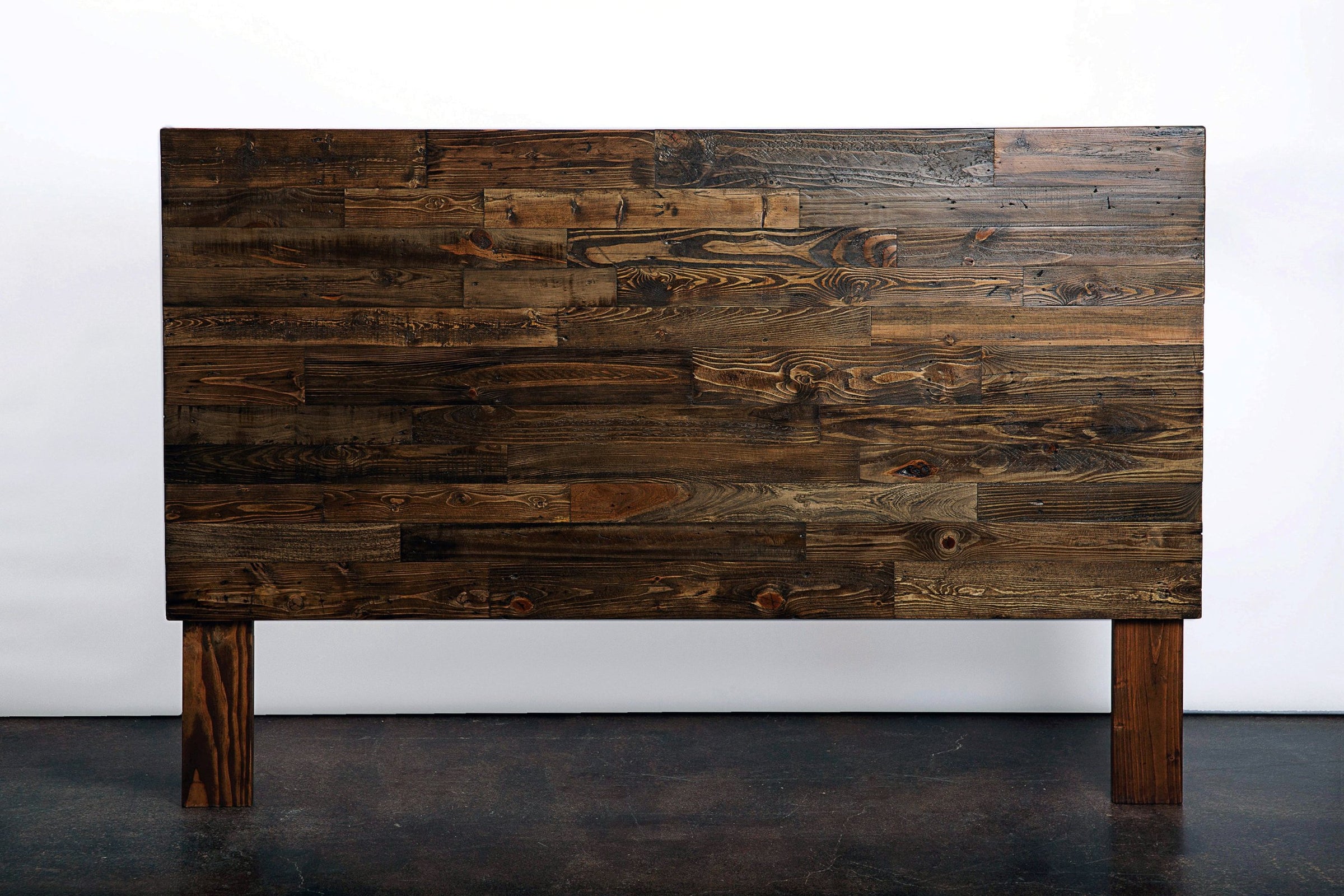 Handcrafted in Arizona, this rustic headboard features a patchwork of dark brown reclaimed wood planks on sturdy wooden legs. Sustainable reclaimed wood furniture, each piece showcases enduring quality and unique artisan charm.