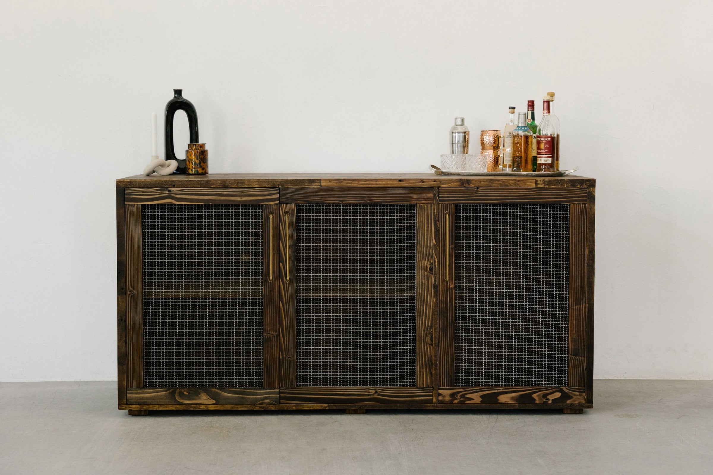 Handcrafted in Arizona, this reclaimed wood sideboard features mesh doors and showcases enduring quality. Styled as a narrow bar table, its top displays curated barware for a refined, sustainable touch to your home or restaurant.