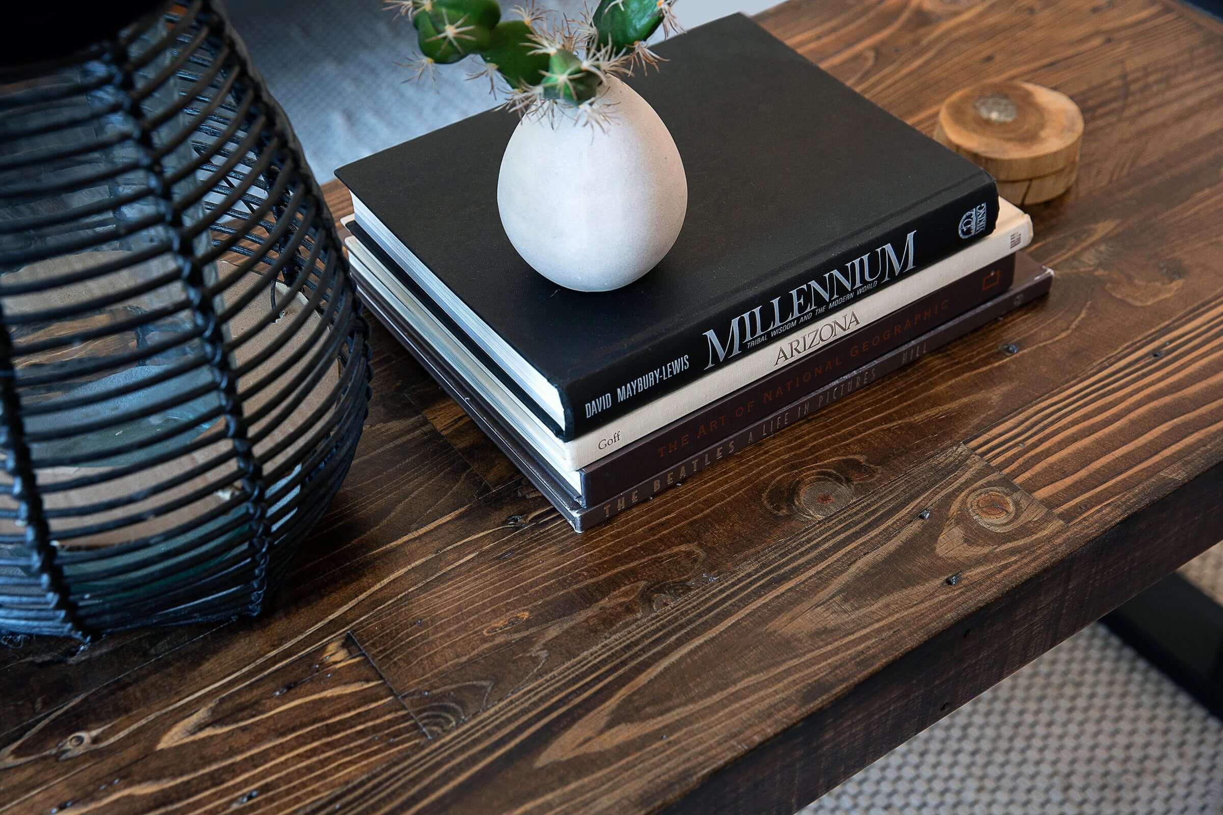 This handcrafted reclaimed wood coffee table showcases enduring quality, featuring a potted cactus, Arizona-themed books, a wooden container, and a woven lantern—perfect for homes seeking sustainable furniture design.