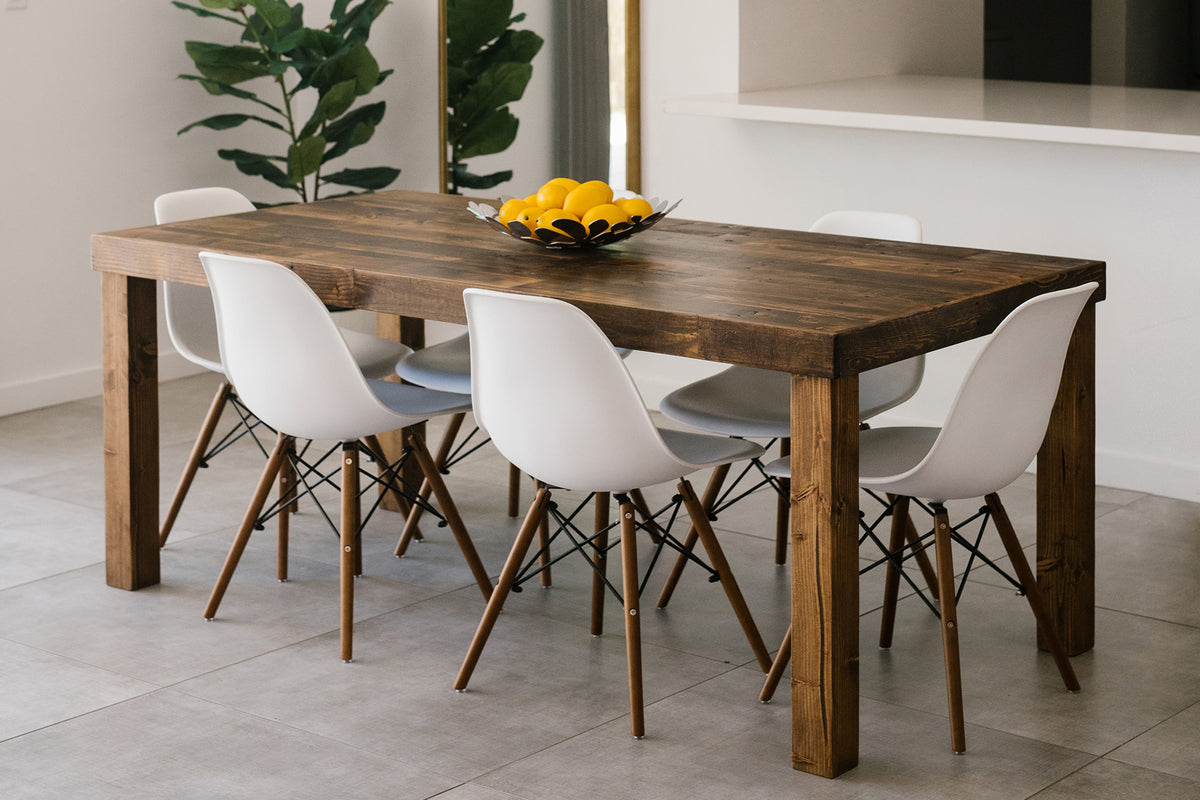 Modern dining area featuring a handcrafted reclaimed wood dining table with six white chairs, wooden legs, and a bowl of lemons; ideal for minimalist spaces or contemporary homes. Potted plant near white counter.