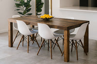 Experience timeless craftsmanship with this Arizona-handcrafted reclaimed wood dining table, paired with six mid-century modern white chairs. A black fruit bowl of lemons and a potted plant accent the tiled floor setting.