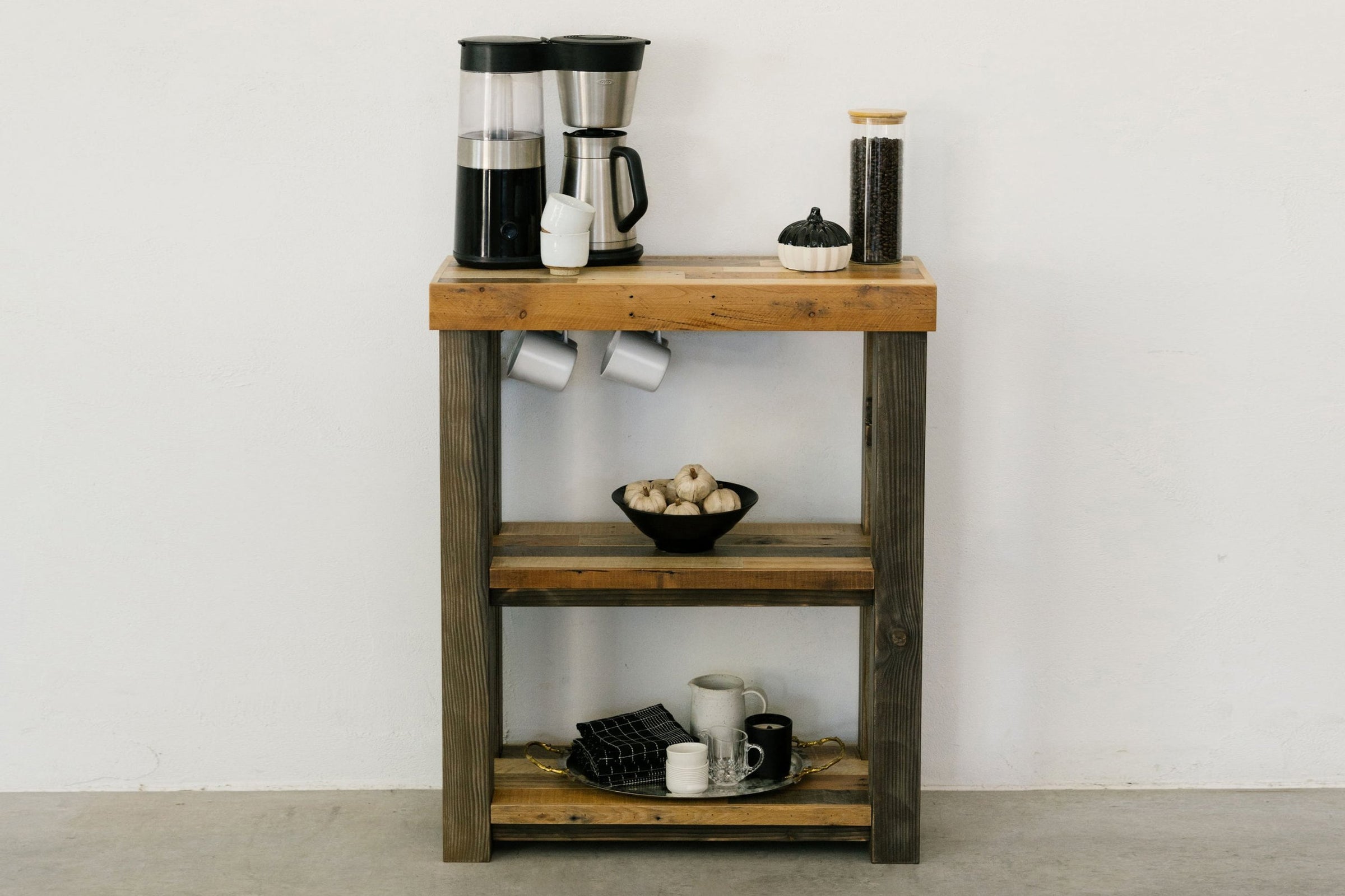 This handcrafted coffee station doubles as a narrow bar-height table, featuring reclaimed wood and sustainable materials. Thoughtful shelves hold a coffee maker, grinder, mugs, and jars—ideal for kitchens or cafes seeking enduring quality.
