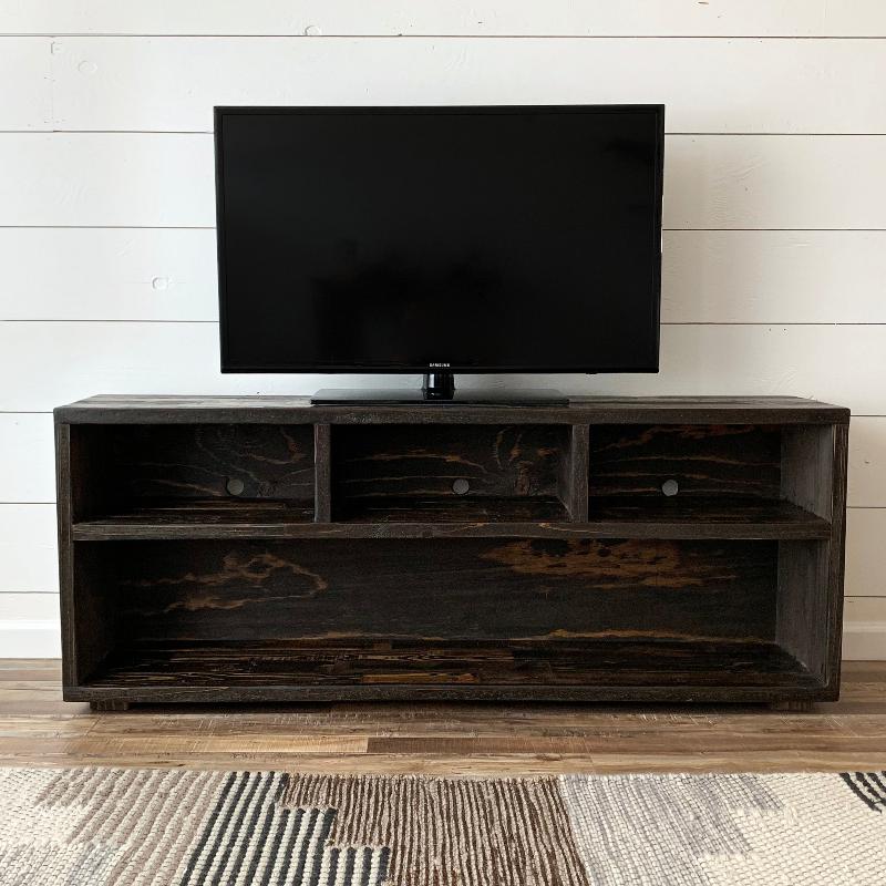 Handcrafted dark reclaimed wood media console with open upper compartments and large lower shelf, supporting a flat-screen TV against a white shiplap wall; suits modern or historic living rooms.