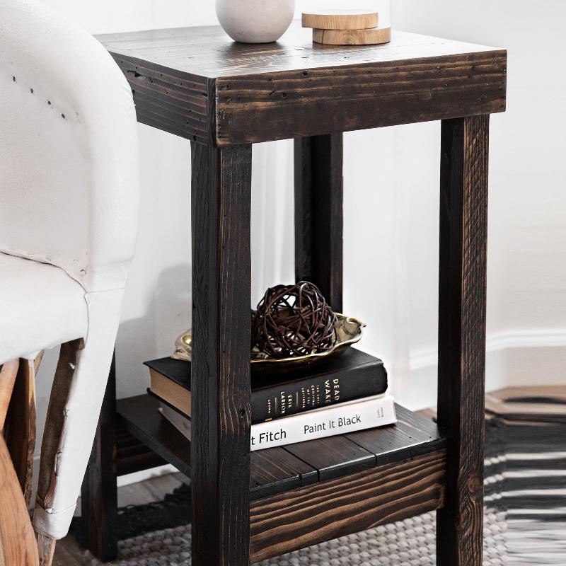 Reclaimed wood side table, handcrafted in Arizona, featuring a lower shelf with books and bowl, plus ceramic vase and wooden lid on top. Perfect for minimalist spaces or historic homes; shown by a white upholstered chair.