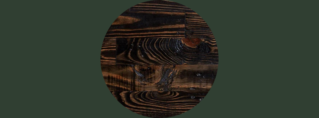 Close-up of handcrafted bar-height dining table made from dark reclaimed wood, showcasing visible grain patterns and swirling textures; ideal for modern cafés or minimalist spaces.