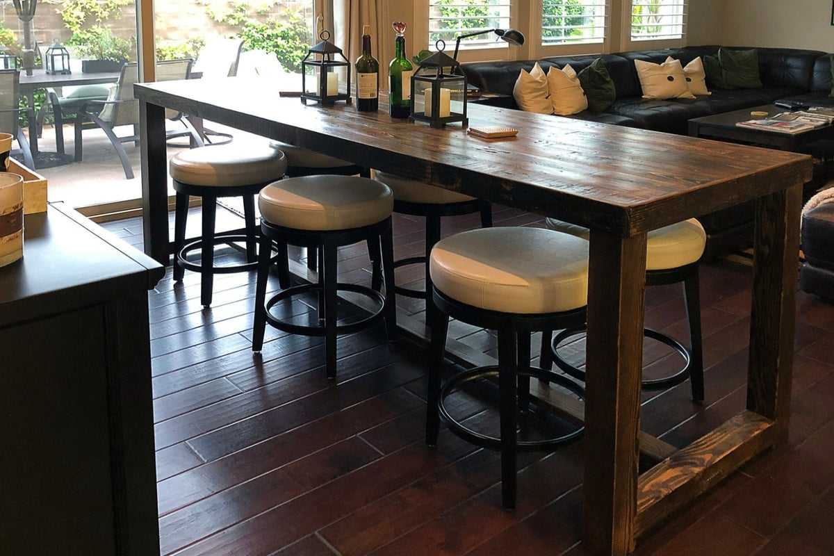 This handcrafted reclaimed wood bar-height table, paired with four round cushioned barstools, showcases enduring quality and sustainable materials. Ideal as a kitchen island or restaurant table in modern spaces with abundant natural light.