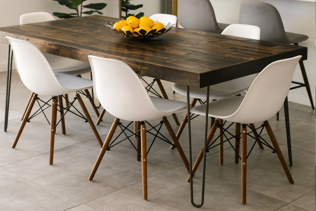 This handcrafted dining table showcases a dark reclaimed wood top and sturdy steel hairpin legs, paired with six white chairs. Perfect as a narrow restaurant table or kitchen island. A black bowl of lemons adds warmth.