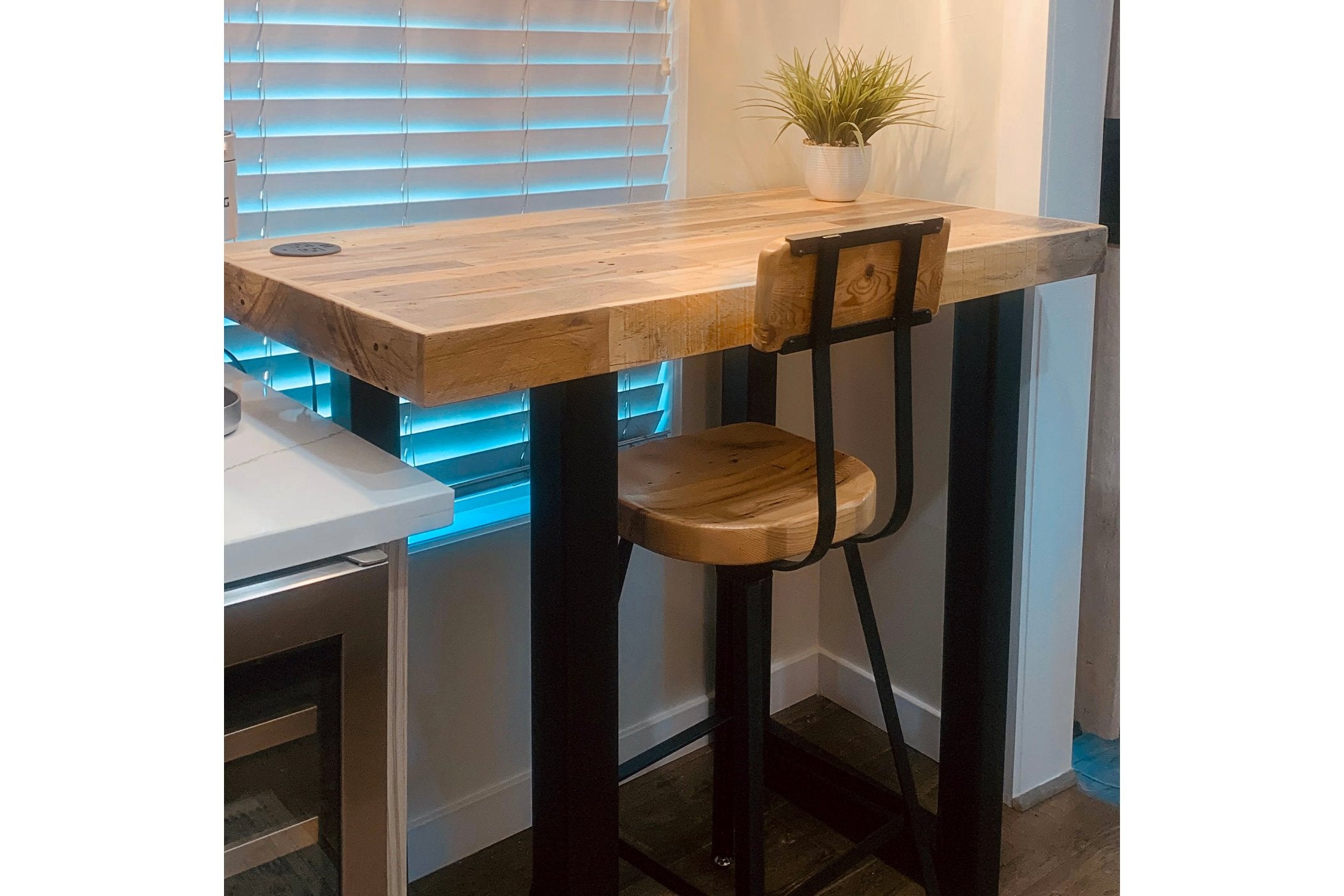 This handcrafted Gunnison bar-height table features a reclaimed wood top and durable industrial steel legs, paired with a matching bar stool. Perfect as a kitchen island or restaurant table, bathed in warm natural light.
