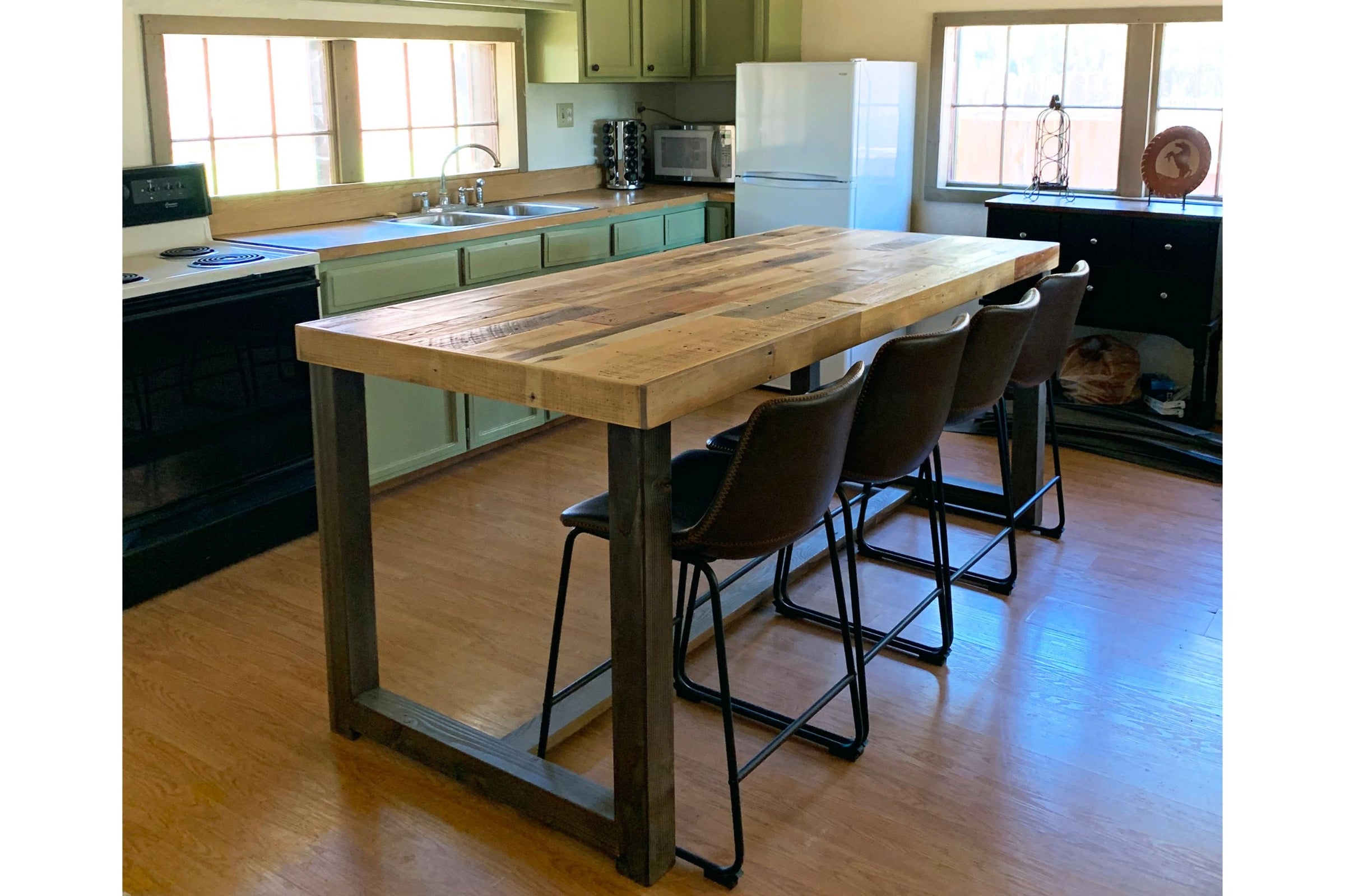 A sunlit kitchen with green cabinetry, a white refrigerator, and a handcrafted Sequoia kitchen island—crafted in Arizona from reclaimed wood with a sturdy steel frame. Four brown bar stools complete this counter-height table.