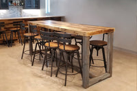 This handcrafted Sequoia bar-height table, made from sustainably sourced wood with a natural finish, is paired with six sleek black metal stools in a modern kitchen. Ideal as a narrow dining or restaurant table.