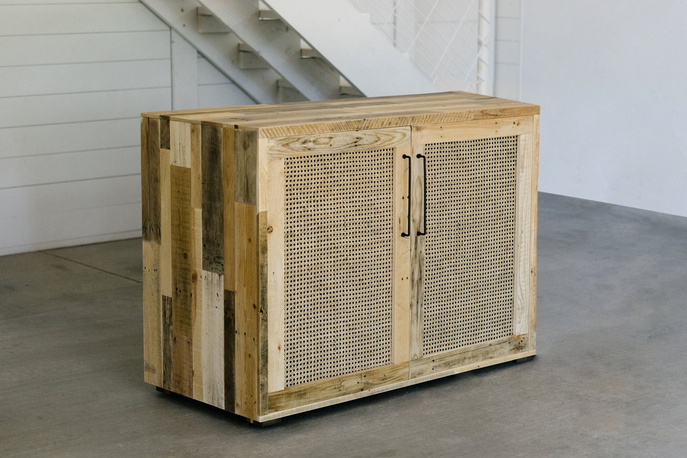 Handcrafted in Arizona, this reclaimed wood sideboard showcases woven cane doors and sleek black handles, elevating any space with enduring quality—perfect for those seeking sustainable and elegant bar table alternatives.