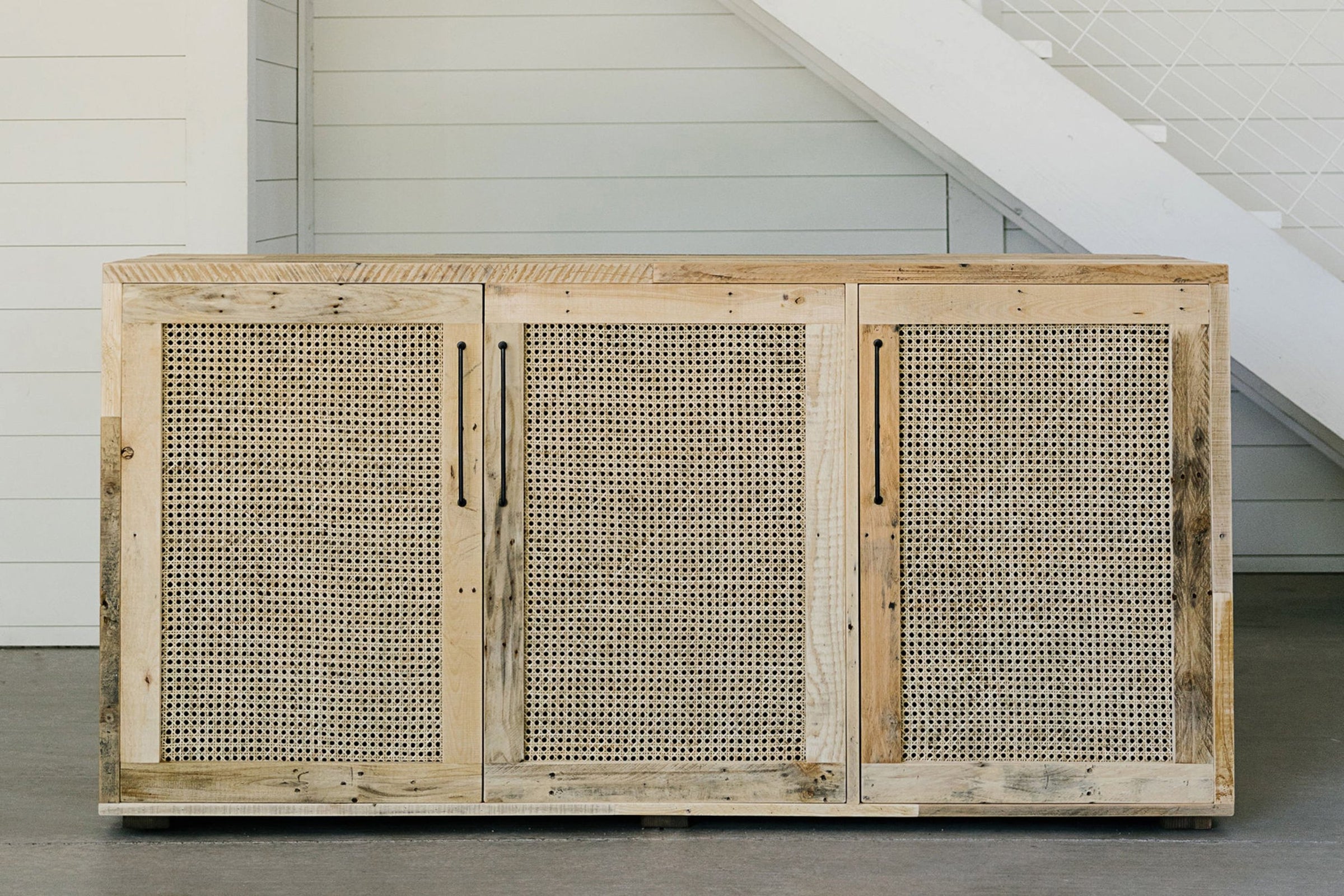 Expertly handcrafted in Arizona, this reclaimed wood sideboard features three cane door panels, offering enduring quality and sustainability. Ideal for dining or as a narrow bar table, it complements modern interiors beautifully.