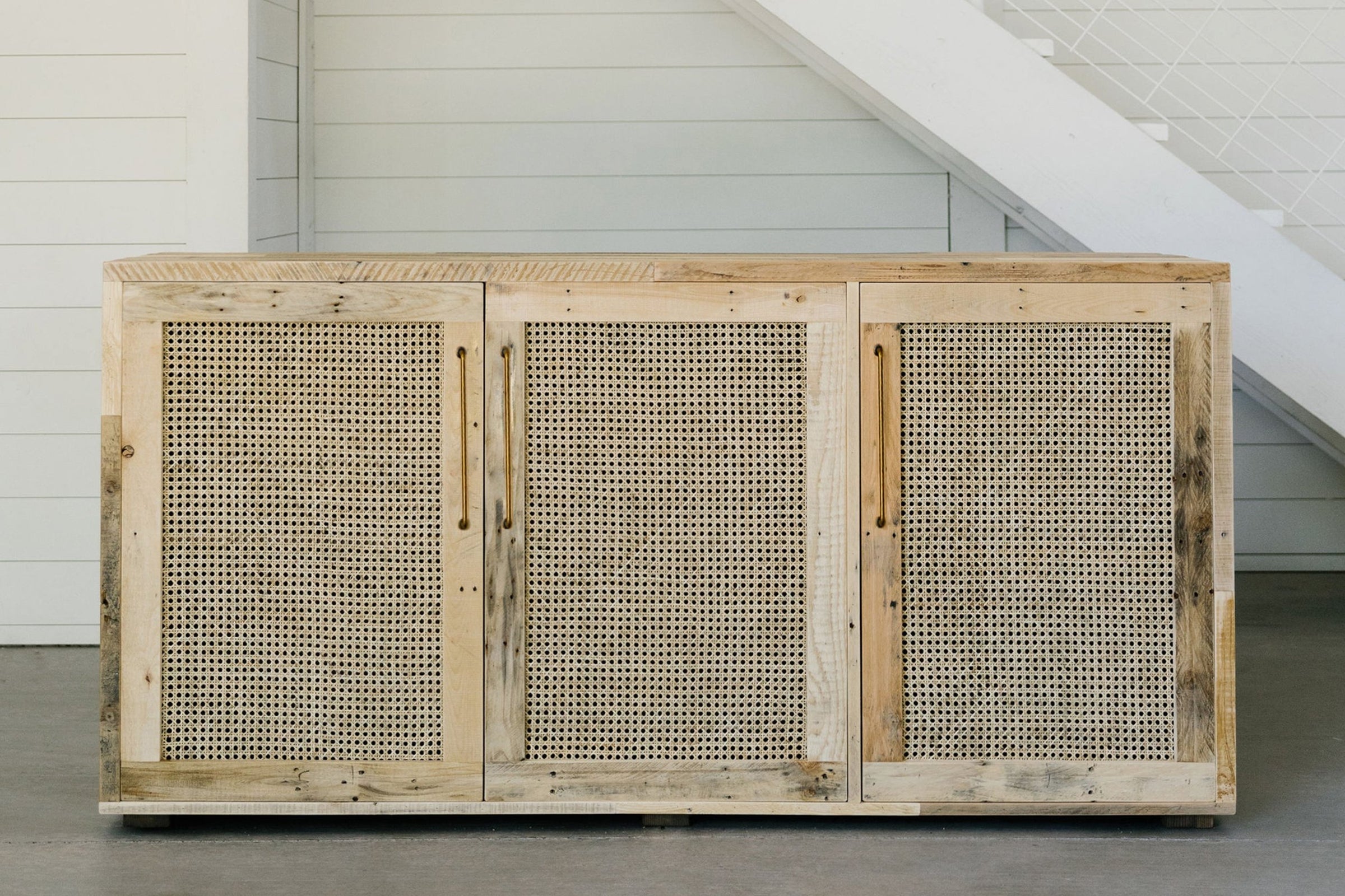 Expertly crafted from reclaimed wood, this sideboard features three woven rattan doors and offers a timeless addition to any space. Ideal as a narrow bar table or dining storage, its minimalist design highlights enduring quality.