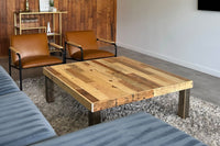 A modern living room showcases a handcrafted Arizona reclaimed wood coffee table, brown leather chairs with sleek black frames, a plush blue sofa, shaggy gray rug, and a quality bar cart—all highlighting enduring reclaimed wood furniture.