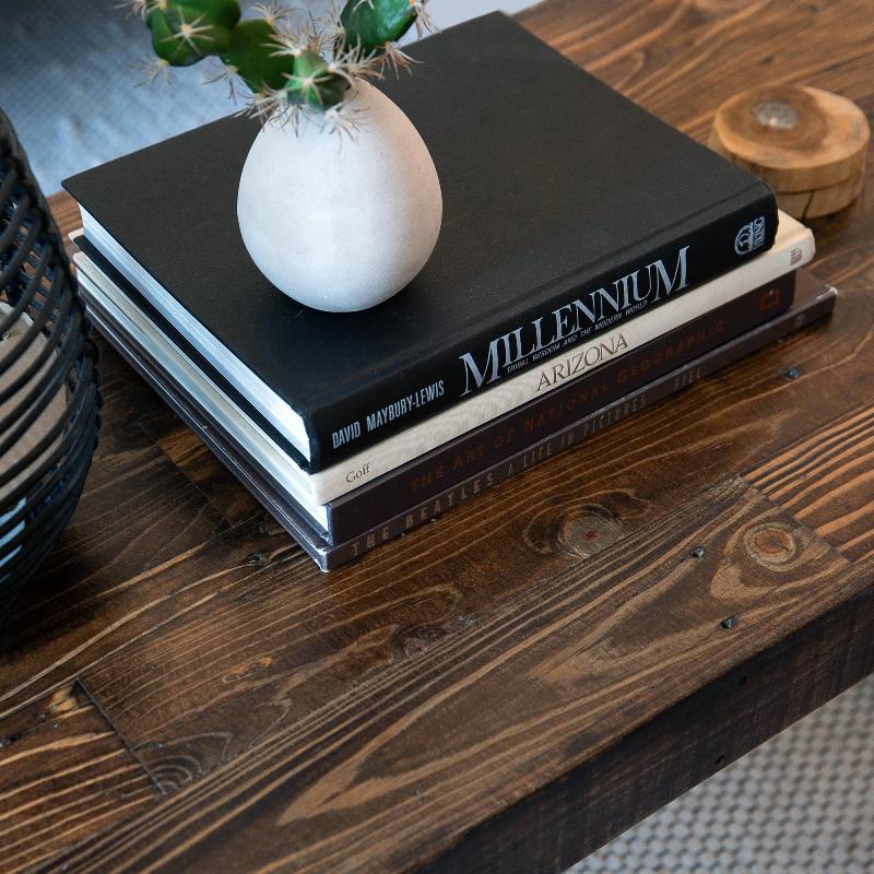 Small white vase with cactus atop books labeled MILLENNIUM and ARIZONA on a rustic, handcrafted reclaimed wood table with dark finish—ideal for historic home or modern café settings.