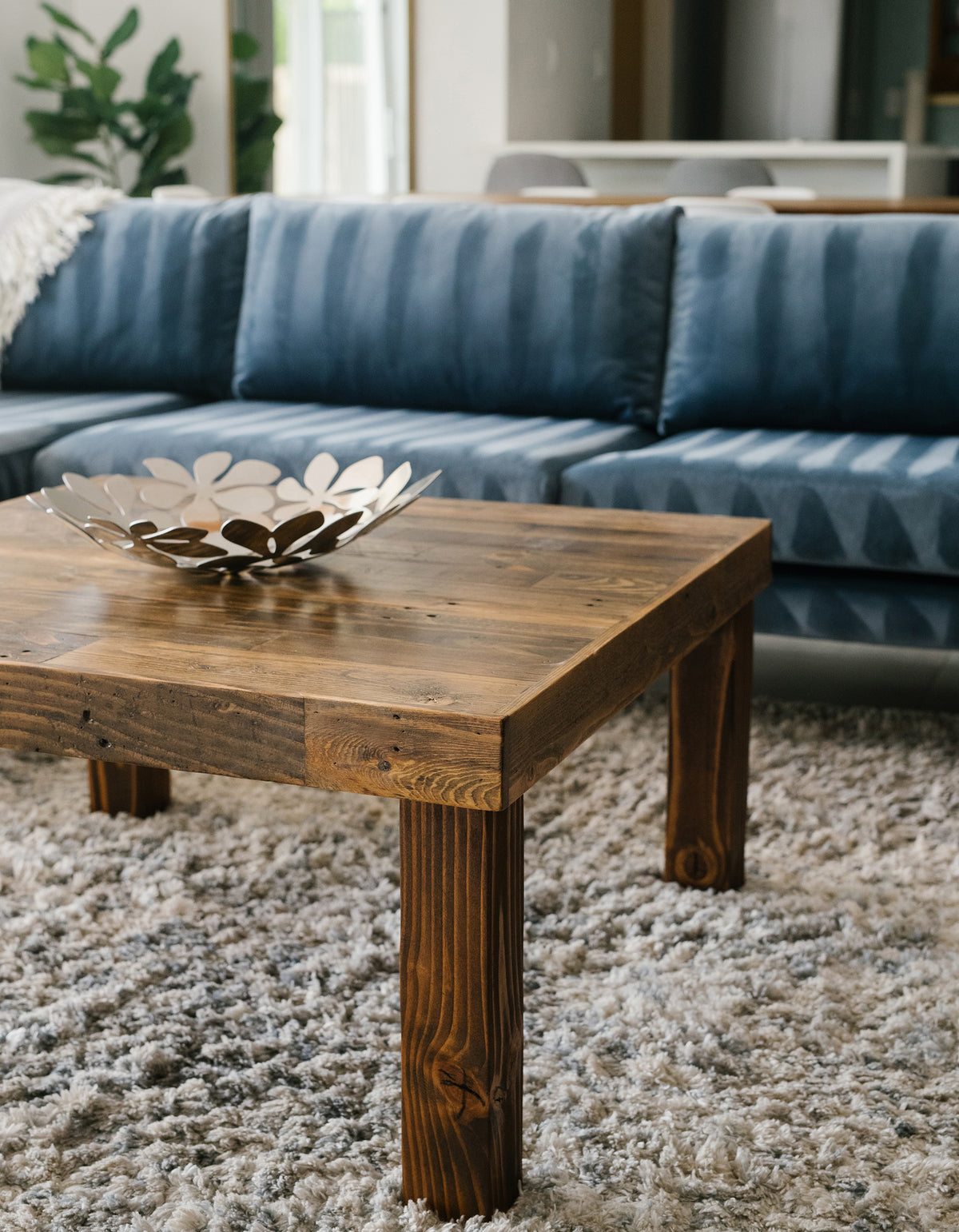 Reclaimed wood coffee table with metallic bowl on textured gray rug, set before a blue sofa. Ideal for modern living rooms; showcases quality craftsmanship and sustainable furniture design.