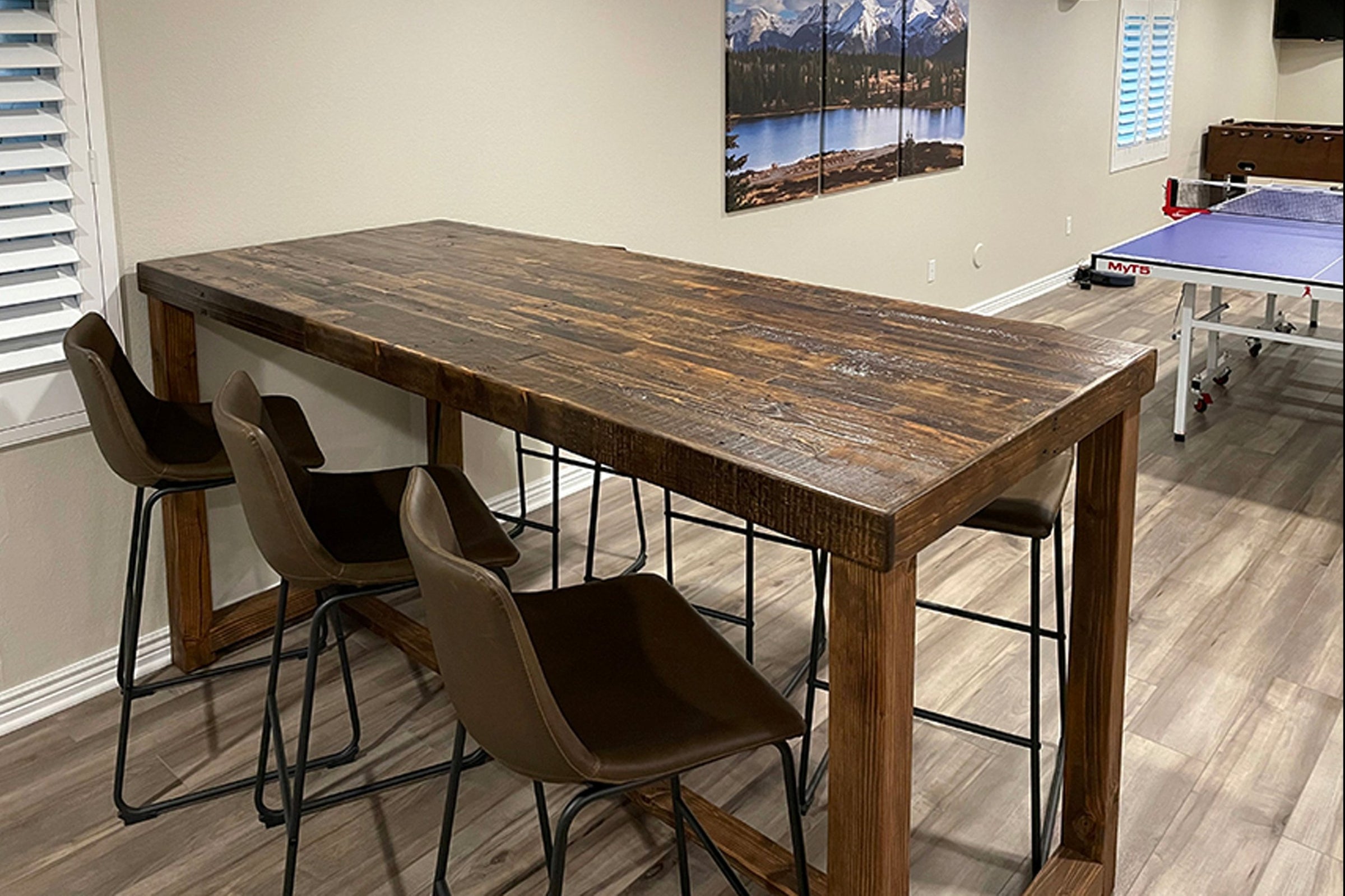 This handcrafted reclaimed wood bar-height table, paired with four brown chairs, anchors a bright room with light wood floors. Durable and sustainable, this premium Arizona-made dining table offers lasting style and eco-friendly appeal.