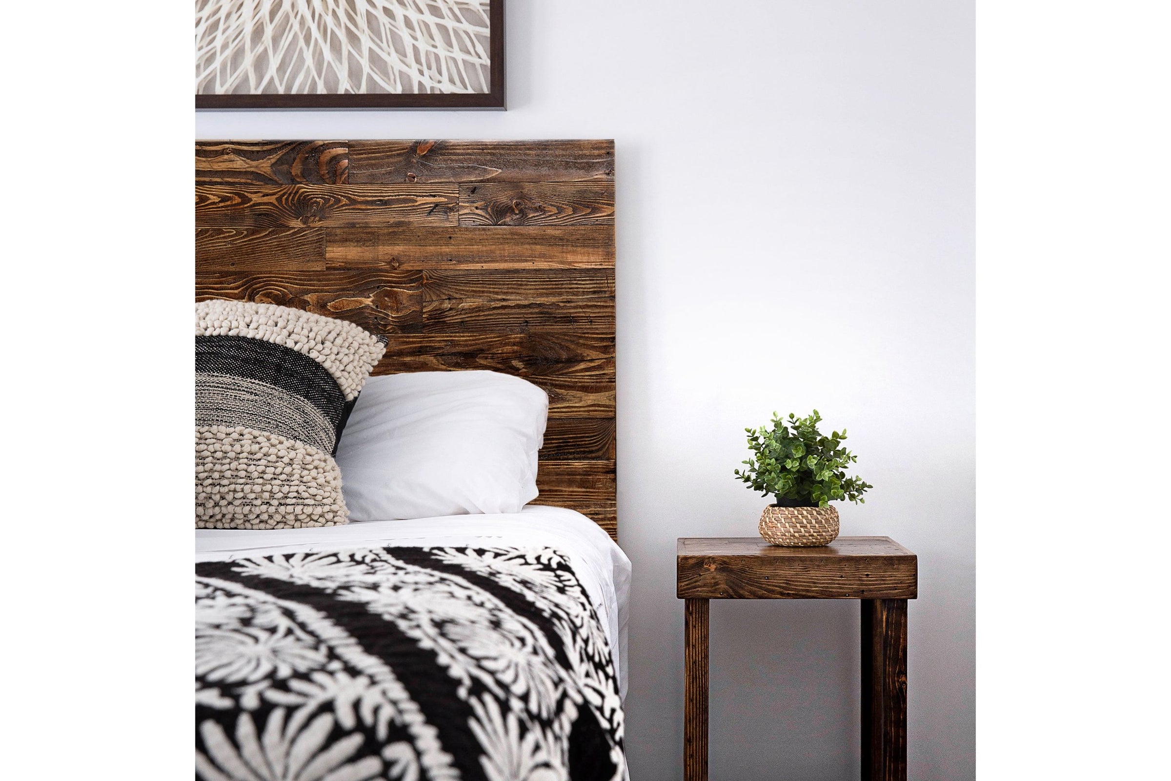 Experience enduring quality in this cozy bedroom, featuring a handcrafted reclaimed wood headboard and matching nightstand. Textured cushions, patterned blanket, and a potted plant complete this sustainable furniture setting.