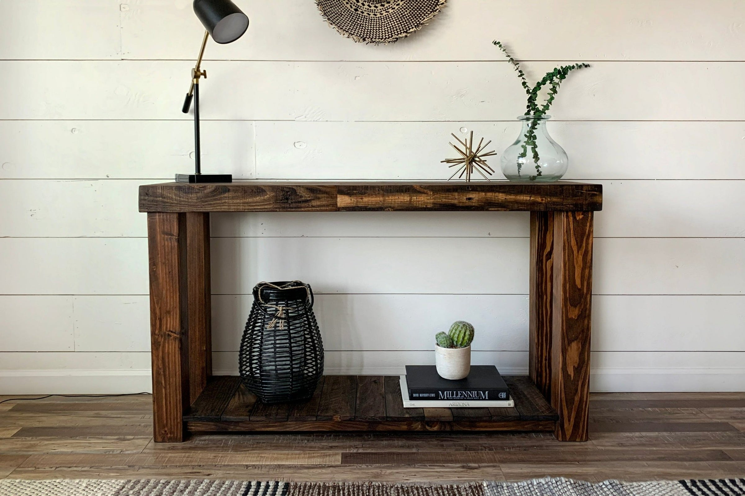 This handcrafted reclaimed wood narrow table stands against a crisp white shiplap wall, showcasing thoughtful decor and a vase with greenery. The sturdy lower shelf features artisan details—part of our sustainable furniture line.