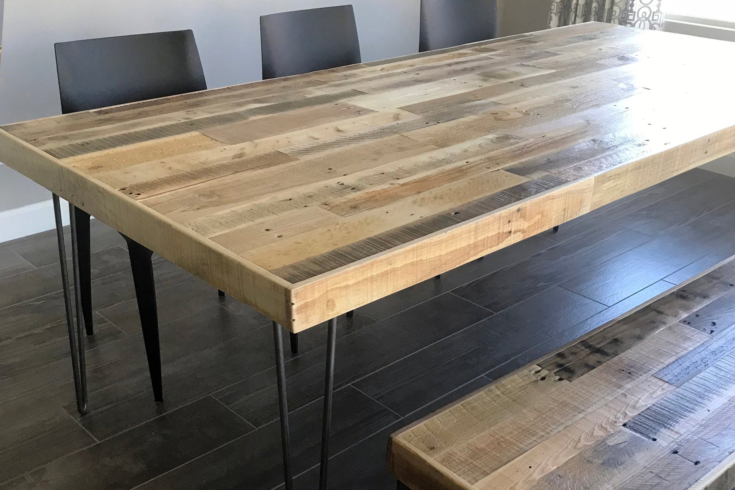 This handcrafted reclaimed wood dining table features a rustic, light-toned surface and sturdy black steel legs. Paired with three sleek black chairs and a matching bench, it’s perfect as a sustainable restaurant or kitchen table.