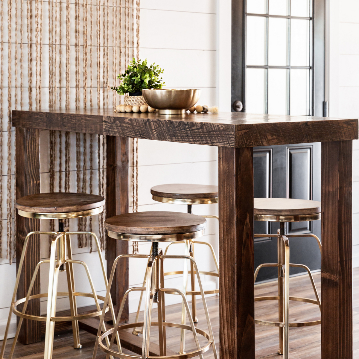 Bar-height dining table handcrafted from reclaimed wood with four barstools featuring gold steel legs. Set in a bright, minimalist space with white walls—ideal for modern cafés or historic homes.