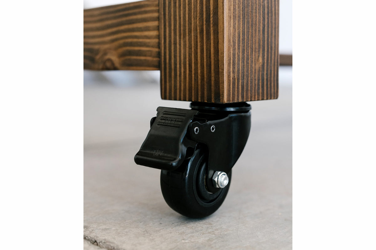 Detailed view of a durable black caster with brake, expertly fastened to the solid reclaimed wood leg, made in Arizona. Exceptional craftsmanship and sustainable design meet enduring utility.