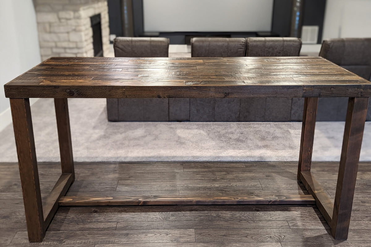 This handcrafted reclaimed wood bar height table has a rustic finish, set on dark wood floors in a home theater. Ideal as a behind-the-sofa bar table in a media room or home bar.
