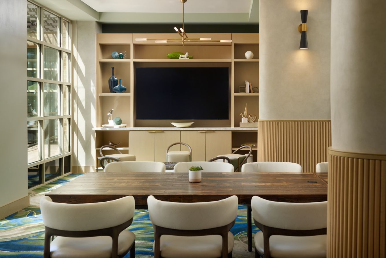 Bright, modern meeting room featuring a handcrafted reclaimed wood conference table—expertly made in Arizona—surrounded by white chairs. Natural light fills the space, accenting sustainable decor and a bar-height table with a steel base.