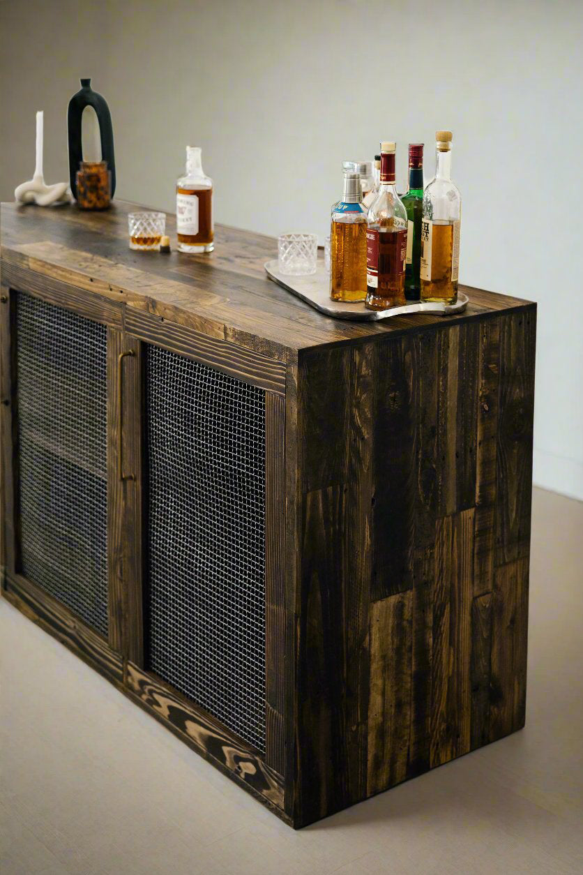 Handcrafted dark wood sideboard with metal mesh doors, featuring a tray of liquor bottles and glasses, black pitcher, and white sculpture; ideal for modern cafés or historic homes seeking reclaimed wood furniture.