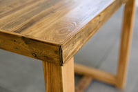Close-up of the corner of a handcrafted, reclaimed wood bar-height table with a Golden Oak finish, showcasing rich grain and sturdy legs. Expertly made in Arizona for lasting quality; ideal as a kitchen island or restaurant table.