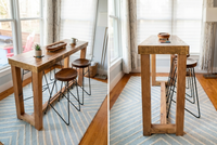 This handcrafted Sequoia bar-height table, made from reclaimed wood in Arizona, pairs with two backless stools. Natural light and hardwood floors accentuate the sustainable craftsmanship—ideal as a kitchen island or narrow dining table.