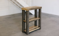 Handcrafted reclaimed wood console table with three shelves and natural finish on concrete floor by white staircase; ideal for modern café, minimalist space, or historic home. Sustainable furniture made in Arizona.