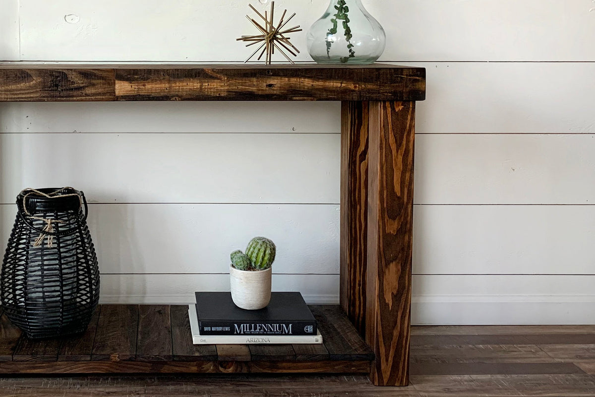 This handcrafted Arizona reclaimed wood narrow console table features exceptional craftsmanship and enduring quality. Accented with a vase, gold starburst, woven lantern, cactus, and books.