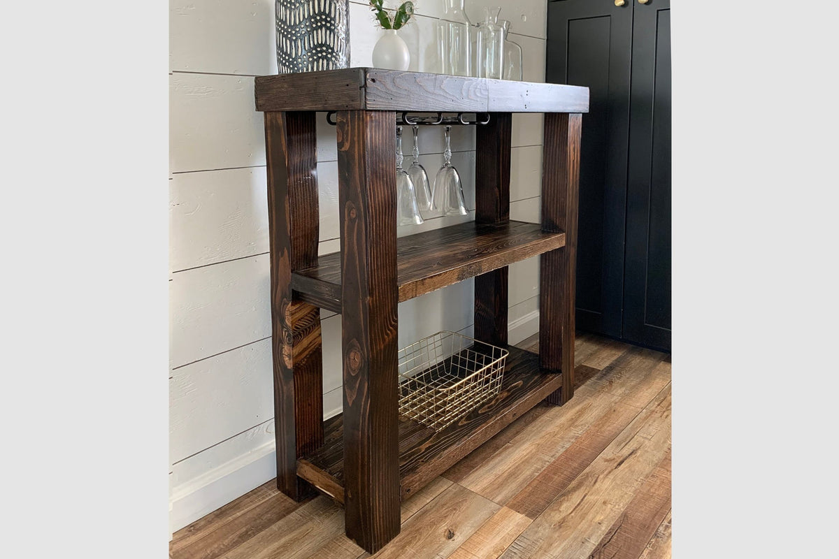 This handcrafted reclaimed wood bar cart features artisan-quality craftsmanship, a top shelf for glassware and decor, ample storage, and a wine glass rack. 