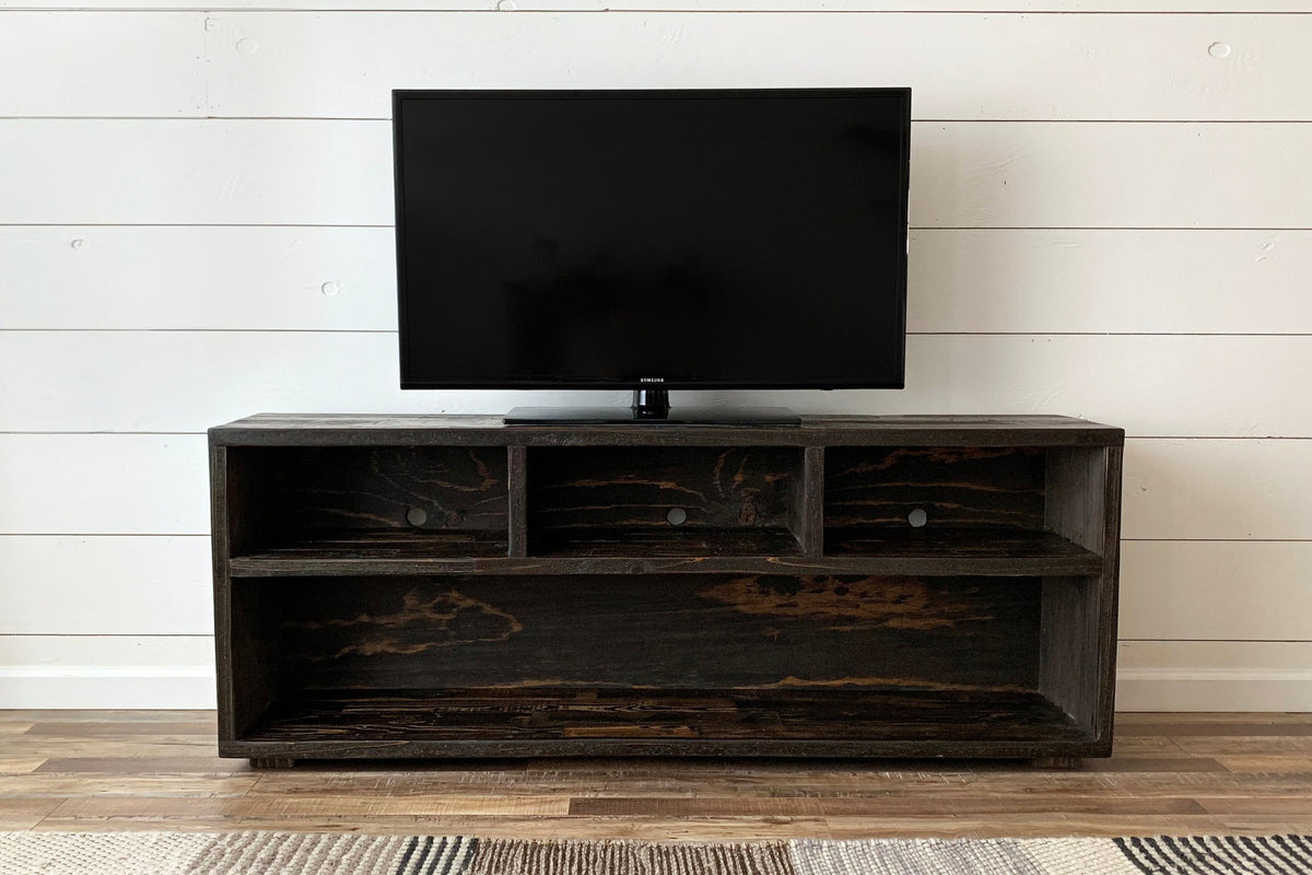 A flat-screen TV rests on a handcrafted reclaimed wood console with open shelving, set against a white shiplap wall. This sustainable media console highlights enduring quality and elevates your space with timeless, eco-friendly design.