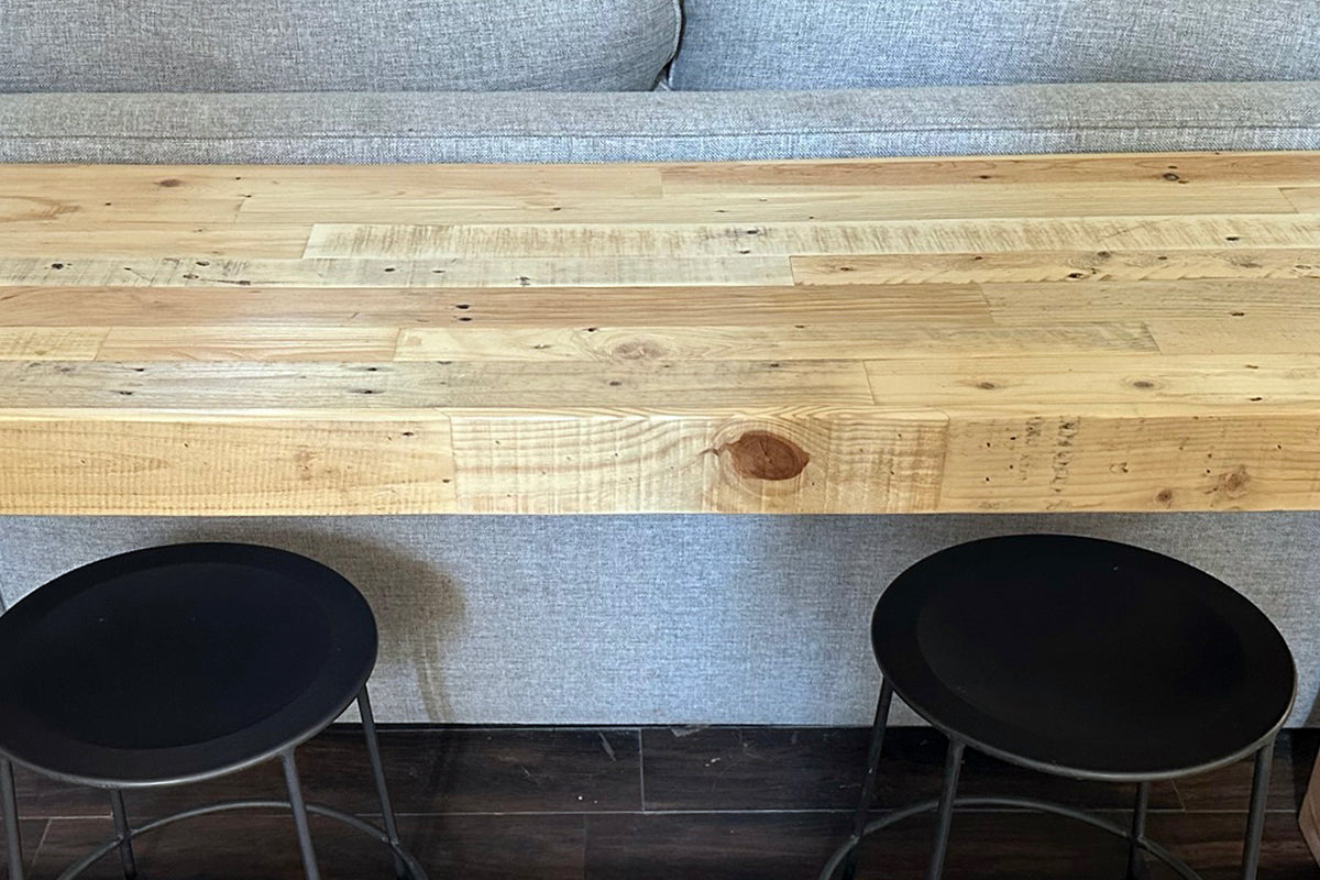 The Gunnison Steel Leg bar-height table, handcrafted in Arizona with a blonde reclaimed wood top and steel base, pairs effortlessly with two black stools—perfect as a kitchen island or restaurant table on a reclaimed wood floor.