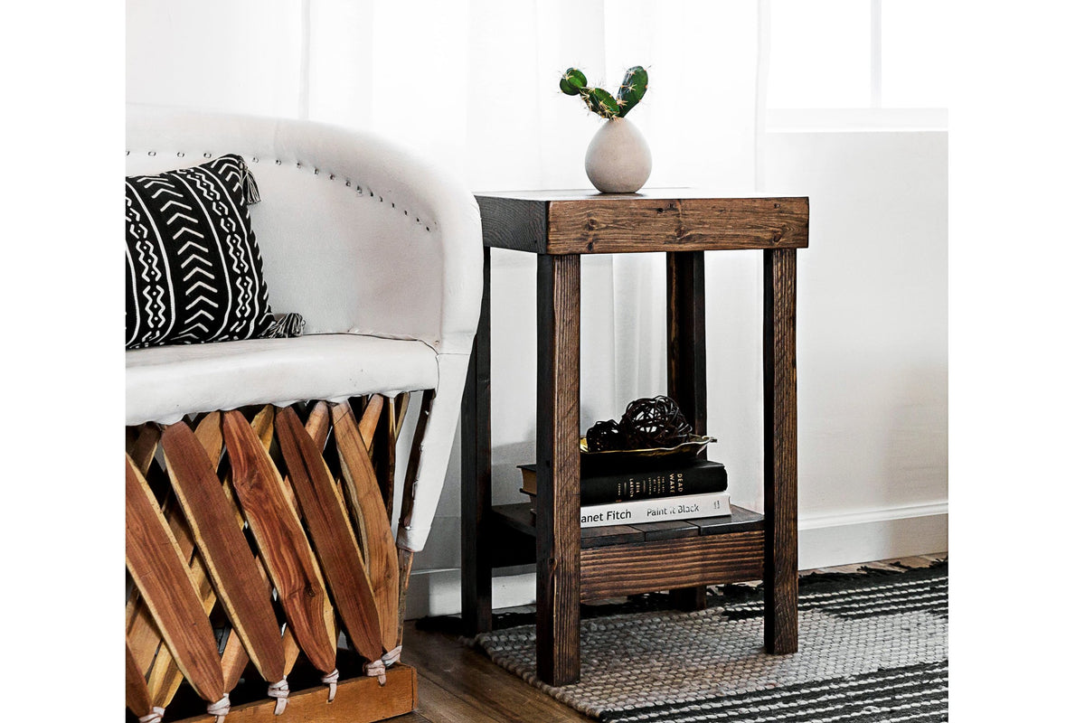 Handcrafted in Arizona, this reclaimed wood narrow side table showcases exceptional craftsmanship and sustainable materials. The sturdy shelf displays a vase and books, complemented by a plush chair and a striped rug.