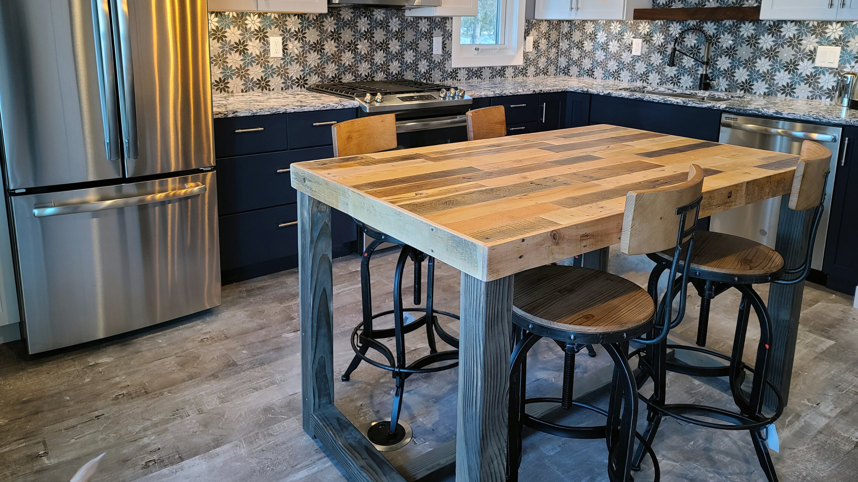 This inviting kitchen showcases a handcrafted reclaimed wood kitchen island—ideal as a counter-height dining table—paired with sleek stainless steel appliances and artisan navy cabinetry, all warmly illuminated by pendant lighting.