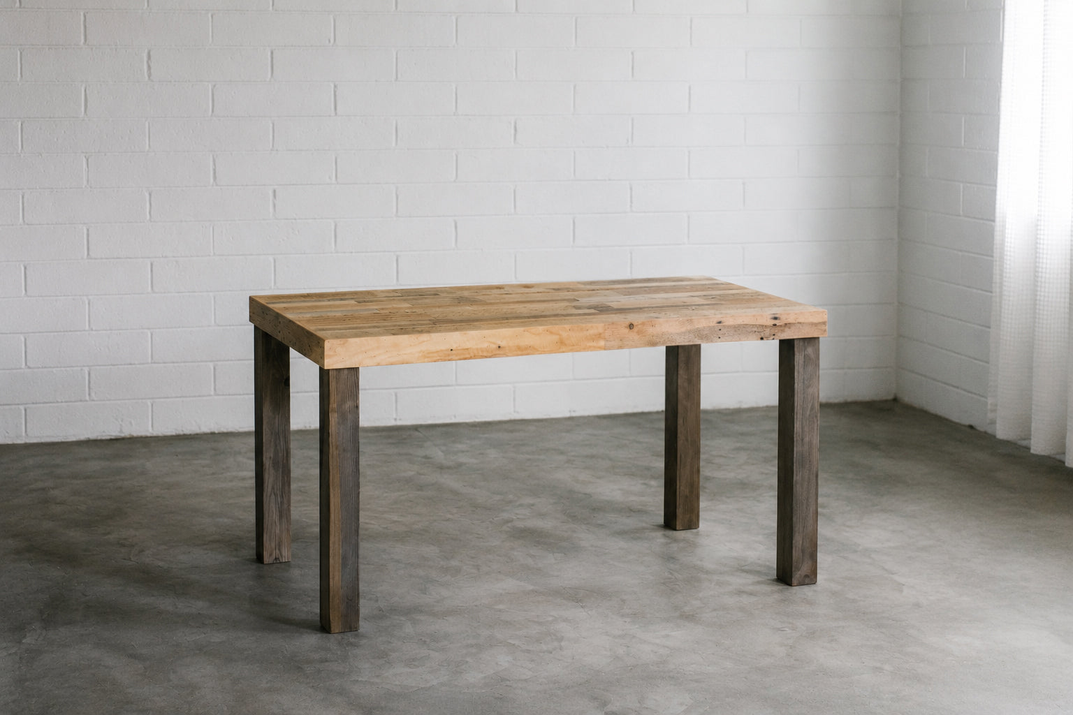 Solid reclaimed wood desk with grey legs against a white brick wall. Handmade by Kase Custom.