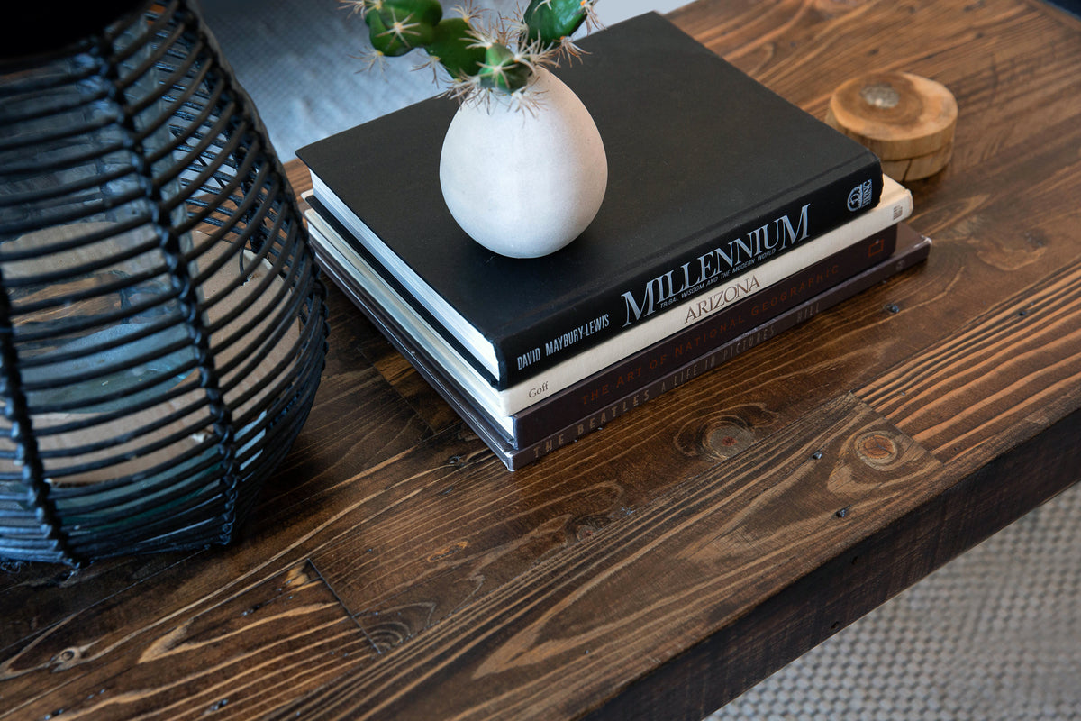 Showcasing timeless craftsmanship, this reclaimed wood coffee table features a sustainable design with a black lantern, a cactus in a small vase, and curated books atop a textured rug—ideal for refined reclaimed wood furniture décor.